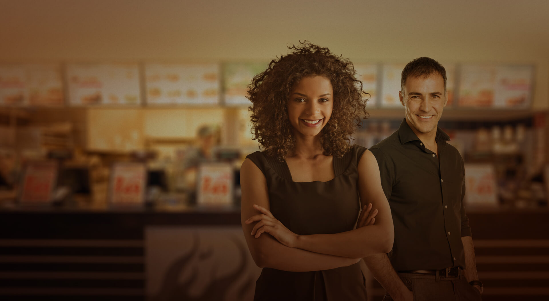 Banner com um homem e uma mulher de braços cruzados, sorridentes com fundo distorcido de um restaurante.